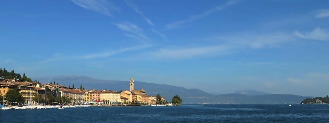 Trip Rumänien beliebte Urlaubsziele am Gardasee -  Mit einer Fläche von 370 km² ist der Gardasee der größte See Italiens. Es liegt am Fuße der Alpen und erstreckt sich über drei Staaten: Lombardei, Venetien und Trentino. Die maximale Tiefe des Sees beträgt 346 m, er hat eine längliche Form und sein nördliches Ende ist sehr schmal. Dort ist der See von den Bergen der Gruppo di Baldo umgeben. Du trittst aus deinem gemütlichen Hotelzimmer und es begrüßt dich die warme italienische Sonne. Du blickst auf den atemberaubenden Gardasee, der in zahlreichen Blautönen schimmert - von tiefem Dunkelblau bis zu funkelndem Türkis. Majestätische Berge umgeben dich, während die Brise sanft deine Haut streichelt und der Duft von blühenden Zitronenbäumen deine Nase kitzelt. Du schlenderst die malerischen, engen Gassen entlang, vorbei an farbenfrohen, blumengeschmückten Häusern. Vereinzelt unterbricht das fröhliche Lachen der Einheimischen die friedvolle Stille. Du fühlst dich wie in einem Traum, der nicht enden will. Jeder Schritt führt dich zu neuen Entdeckungen und Abenteuern. Du probierst die köstliche italienische Küche mit ihren frischen Zutaten und verführerischen Aromen. Die Sonne geht langsam unter und taucht den Himmel in ein leuchtendes Orange-rot - ein spektakulärer Anblick.